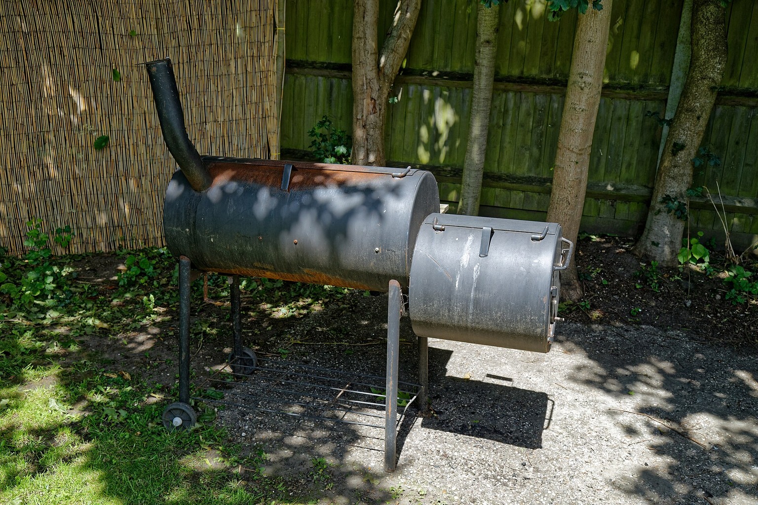 An outdoor barrel-style barbecue with side shelf and cooking chamber.