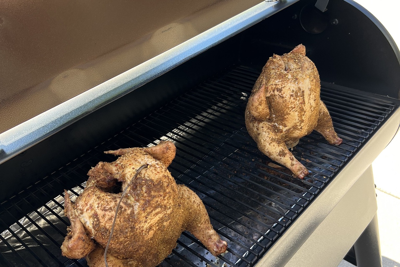 Whole chickens spaced across the grate of a pellet smoker.